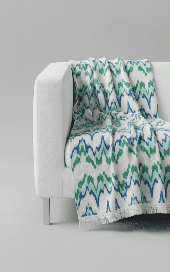 Blue and green ikat patterned oversized throw blanket with fringe border on white sofa
